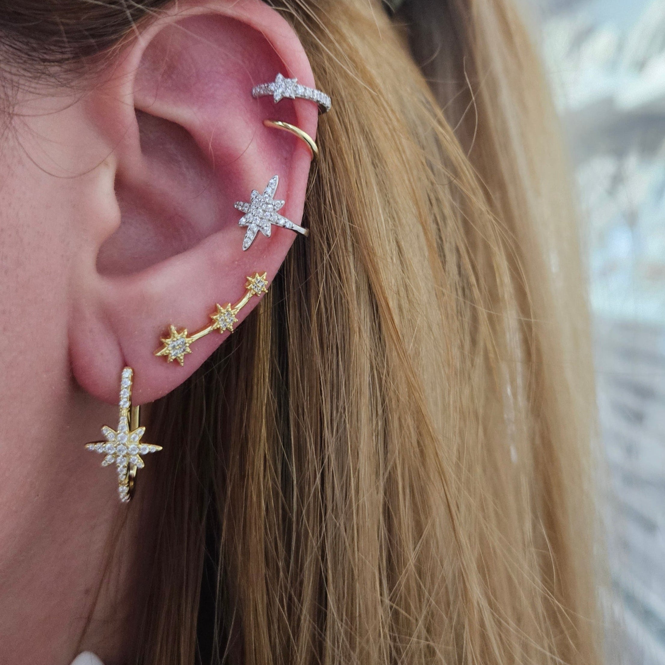 Close-up of an ear with multiple star-shaped earrings against a blurred background