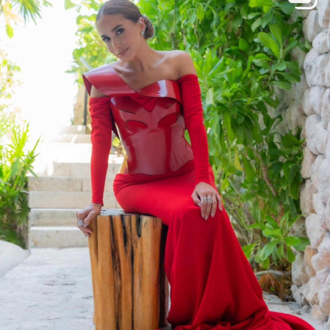 Elegant woman in a red haute couture dress, wearing silver rings with sparkling stones, seated on a wooden bench.