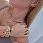 Woman wearing matching gold jewelry set with black and clear stones, including layered necklaces, long drop earrings, stacked bracelets, and statement rings.