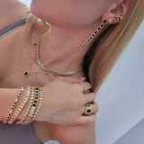 Woman wearing matching gold jewelry set with black and clear stones, including layered necklaces, long drop earrings, stacked bracelets, and statement rings.